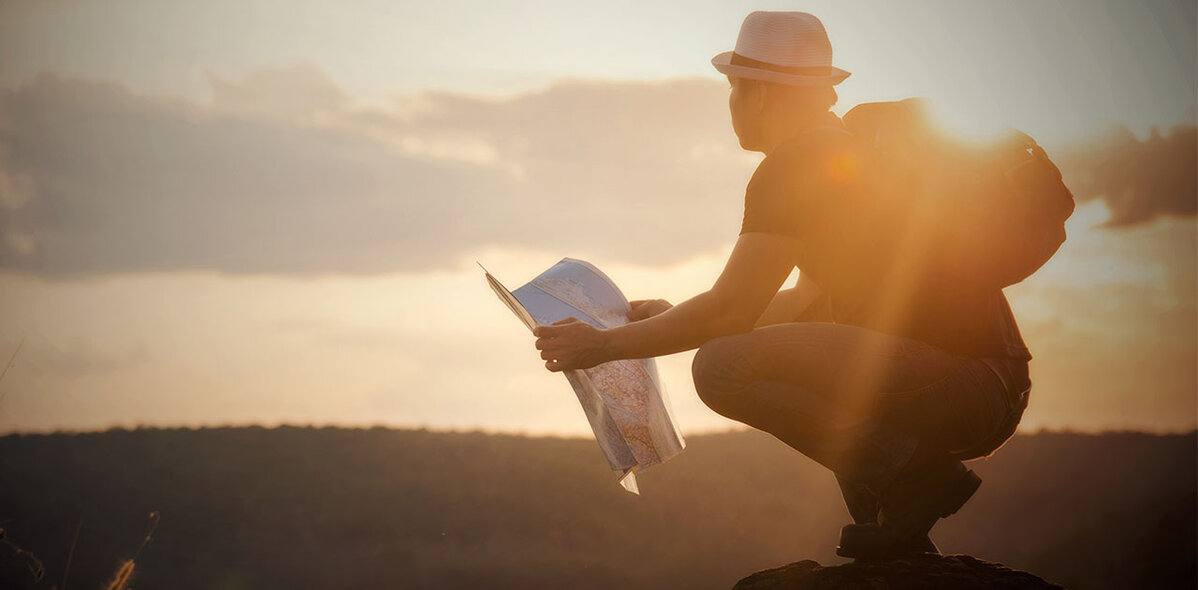 Person stands on a mountain top with a map in the hand